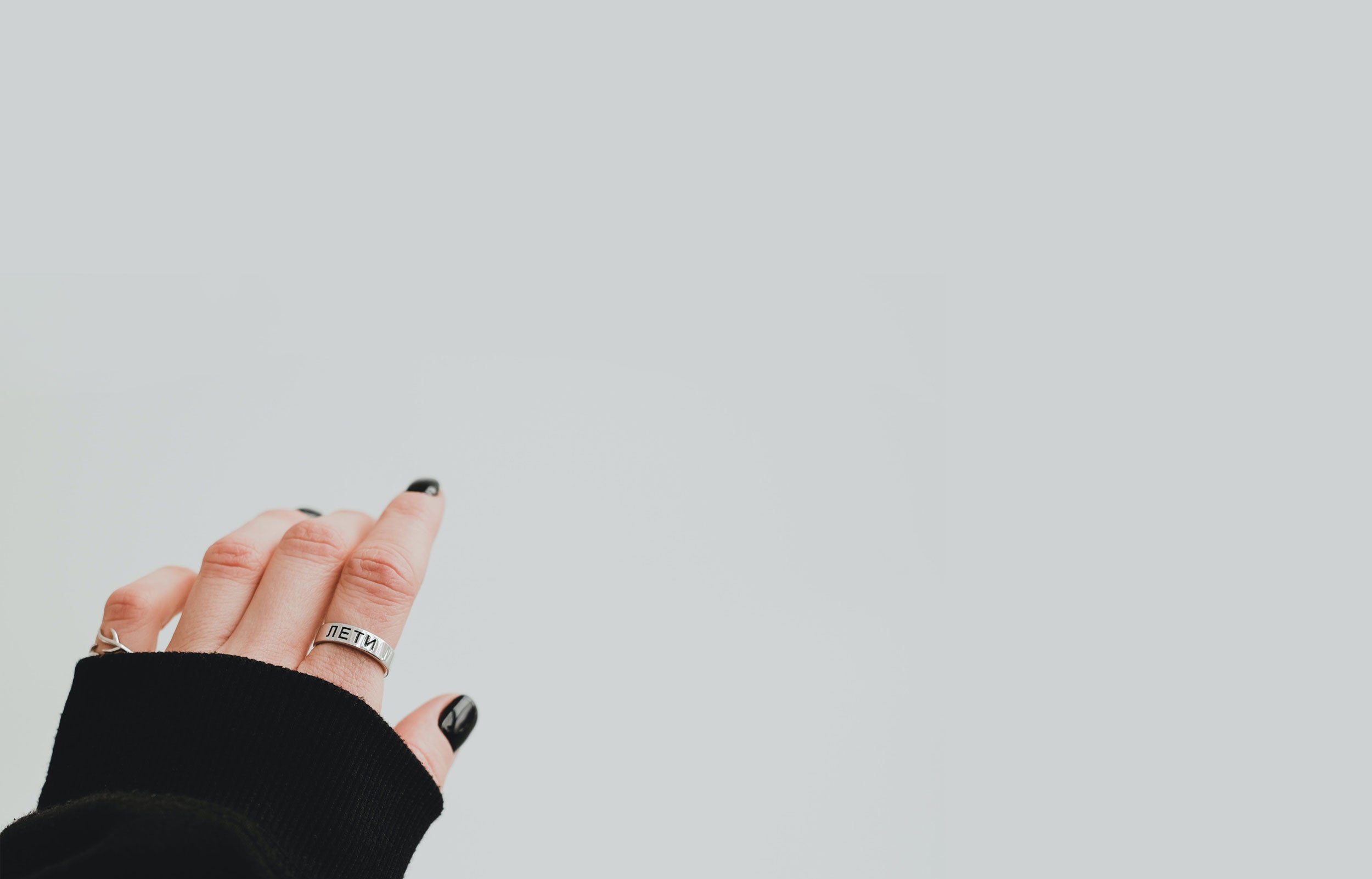 hand with black semi-cured gel nails wearing black jumper on grey background