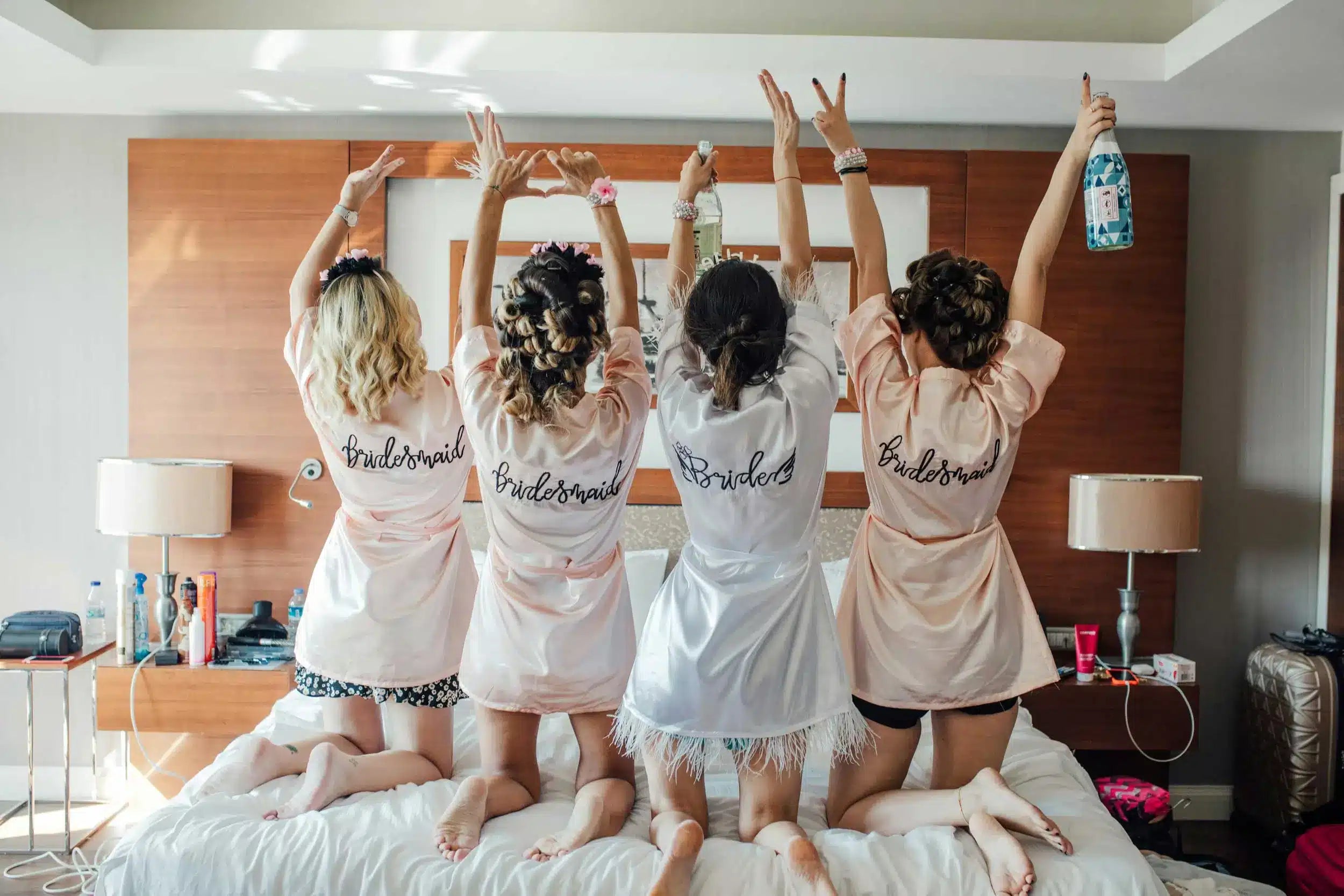 4 girls in bridesmaid robes on a bed with their hands in the air getting ready for wedding