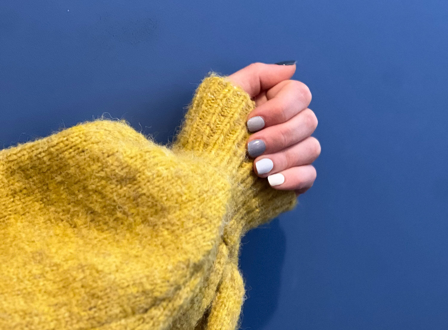 blueberry bush semi-cured gel nails on hand with yellow jumper against a blue wall