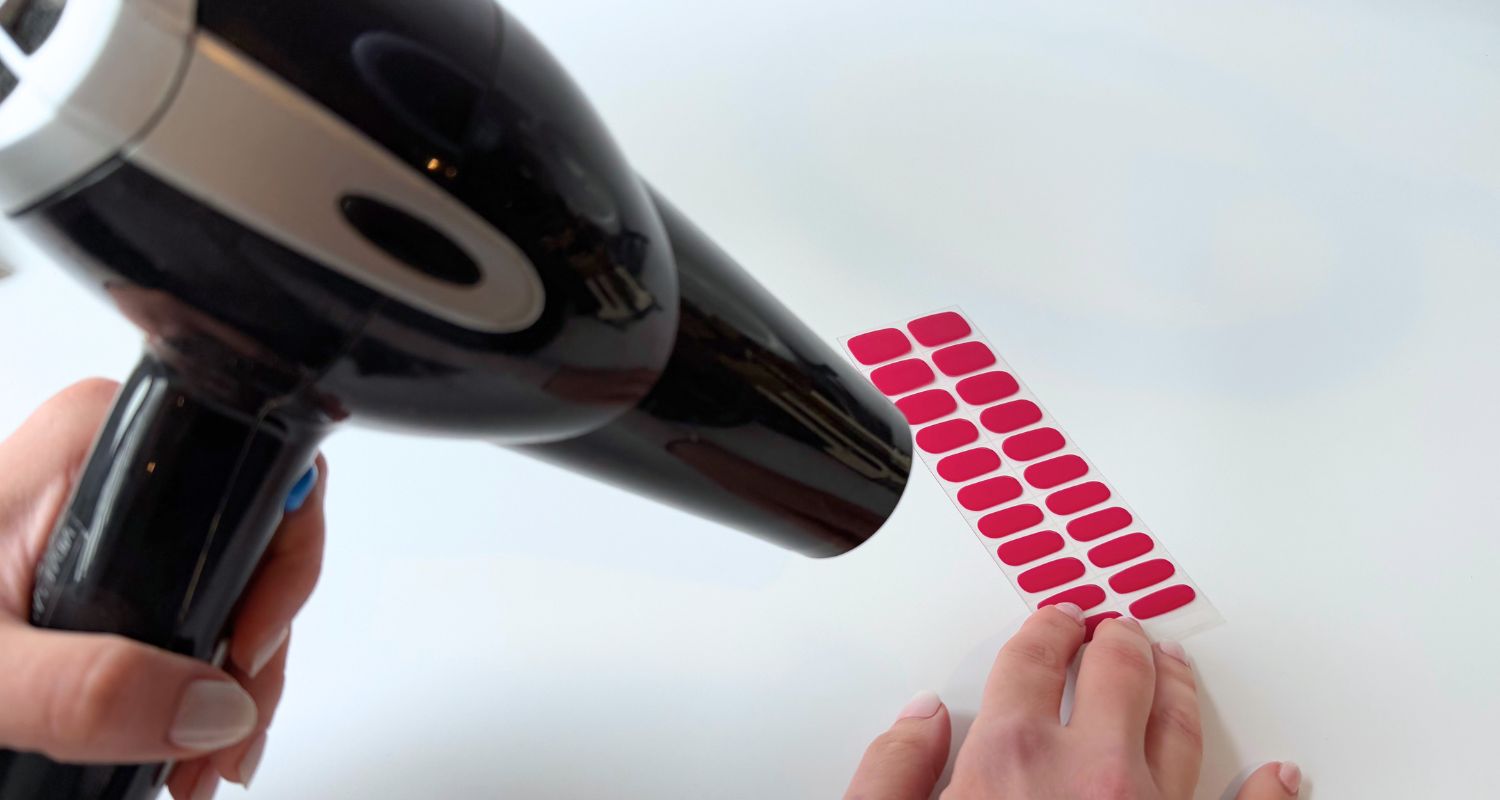Using a hair dryer to warm gel nail wraps before applying them