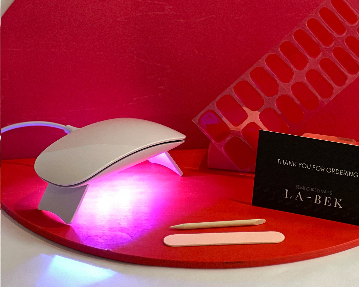 uv lamp on showing light and red semi-cured gel nails on red wooden backdrop