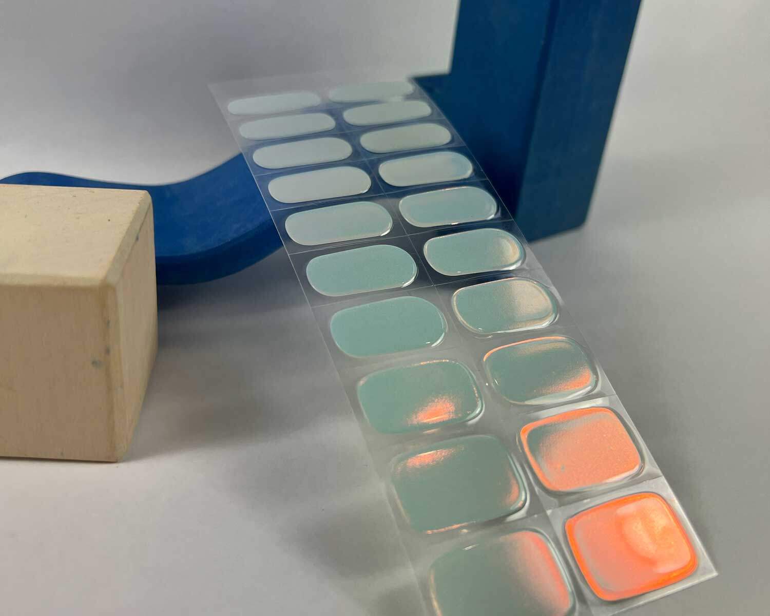 Aurora Mint green blue semi-cured gel nails in mockup to show product against blue wave wooden block with la-bek uv lamp in the background