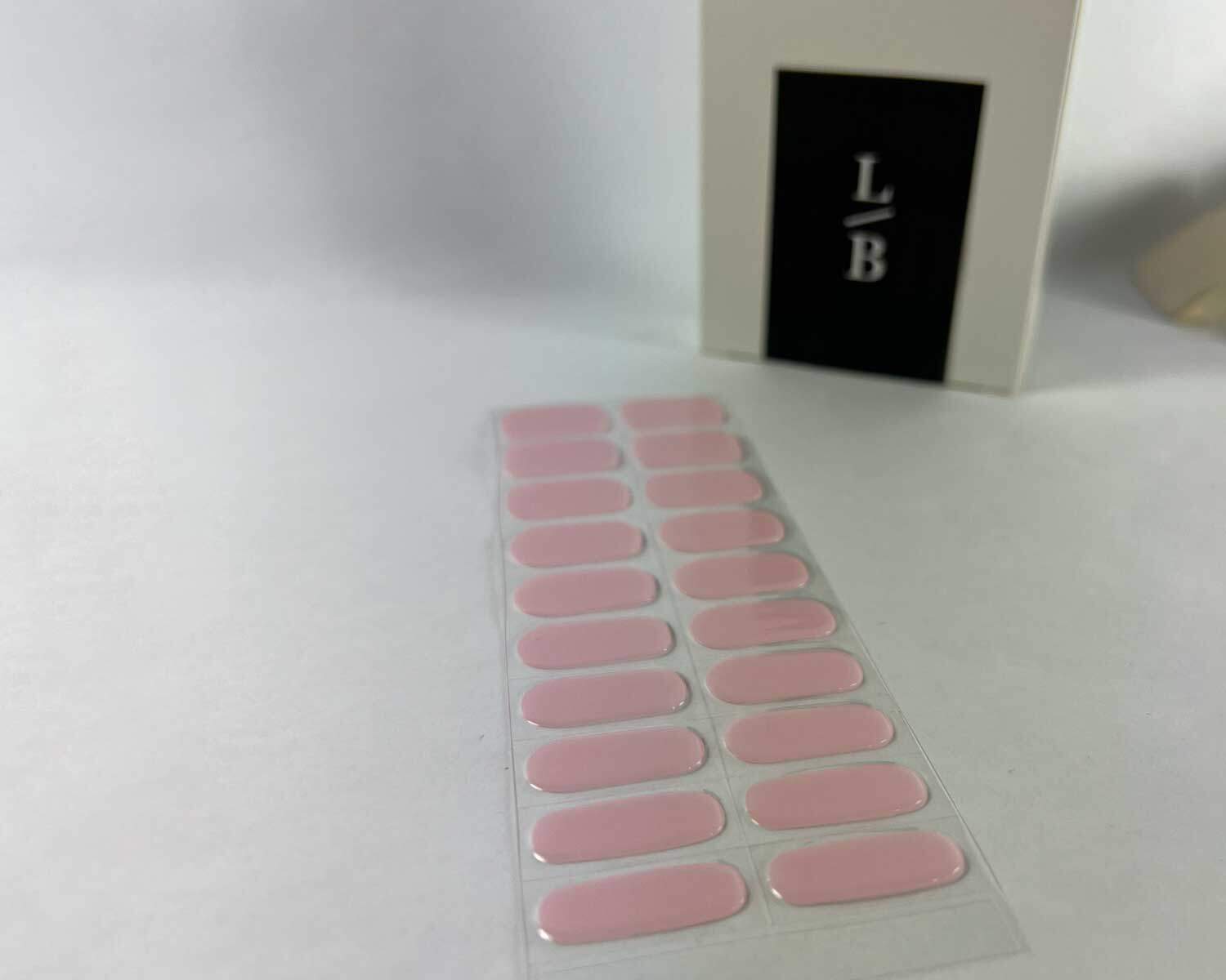 Pale pink power semi-cured gel nails on angle zoomed in on white background with la-bek uv lamp box in the background