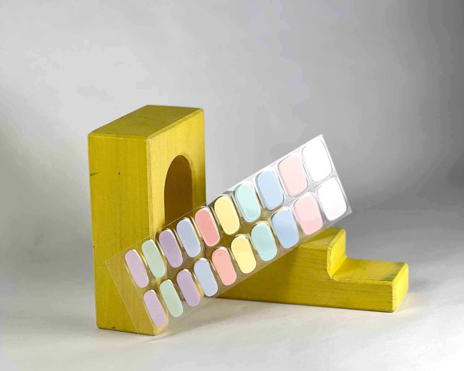 Candy bar rainbow semi-cured gel nails in mockup to show product against yellow wooden blocks with la-bek uv lamp in the background