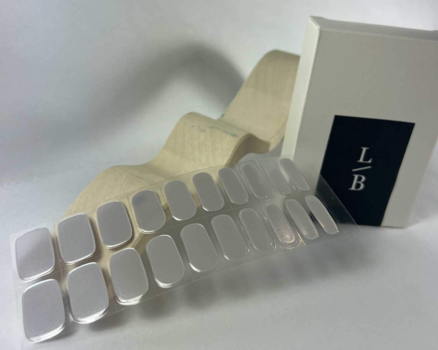 Grey diamond silver semi-cured gel nails in mockup to show product against white wave wooden block with la-bek uv lamp in the background