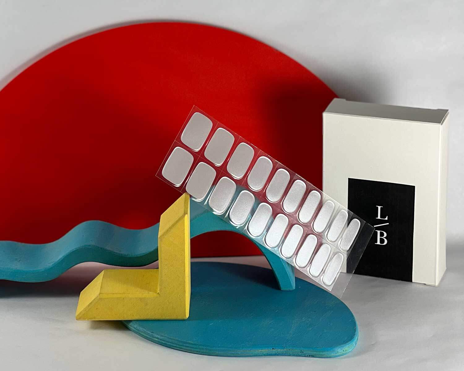 Grey diamond silver semi-cured gel nails in mockup to show product against blue, red and yellow wooden blocks with la-bek uv lamp in the background