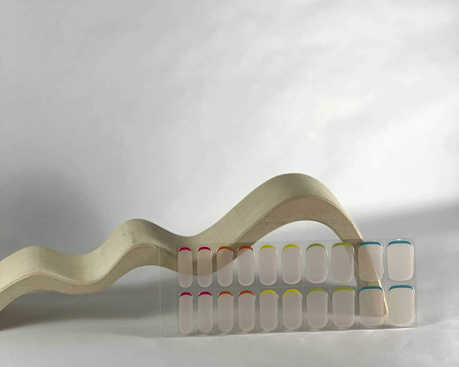 hidden-rainbow-semi-cured-gel-nail-curve Hidden Rainbow semi-cured gel nails in mockup to show product against white wave wooden block with la-bek uv lamp in the background