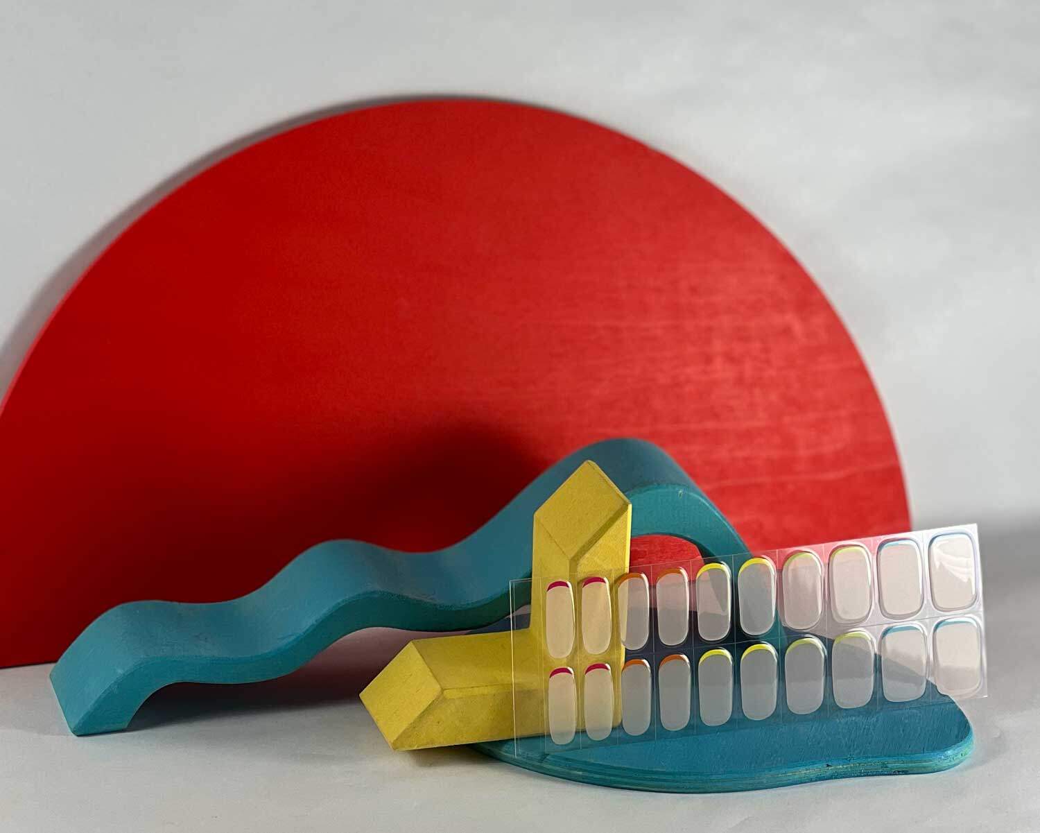 hidden-rainbow-semi-cured-gel-nail-mock Hidden Rainbow semi-cured gel nails in mockup to show product against blue, red and yellow wooden blocks with la-bek uv lamp in the background