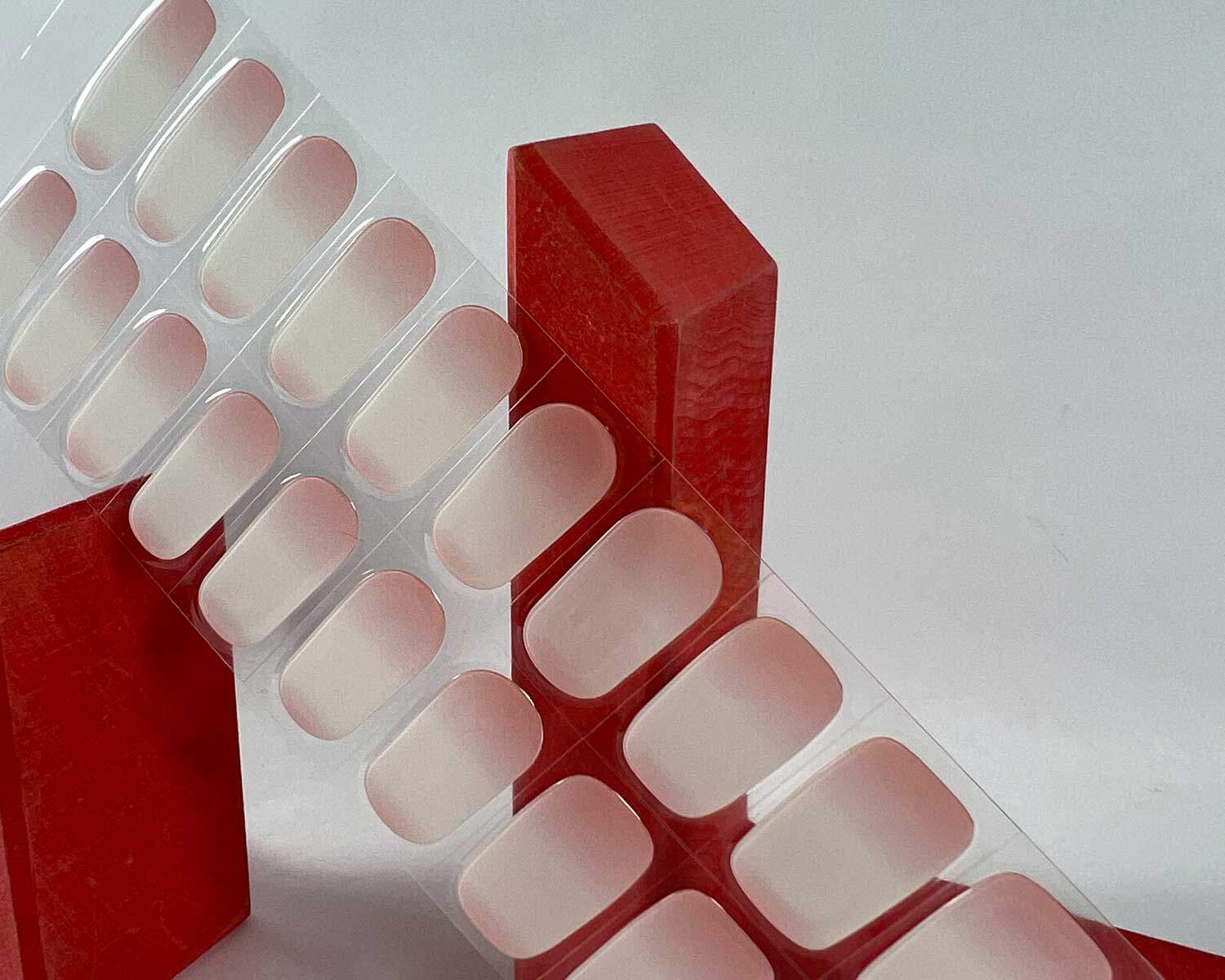 Ombre pink semi-cured gel nails in mockup to show product against red wooden blocks with la-bek uv lamp in the background