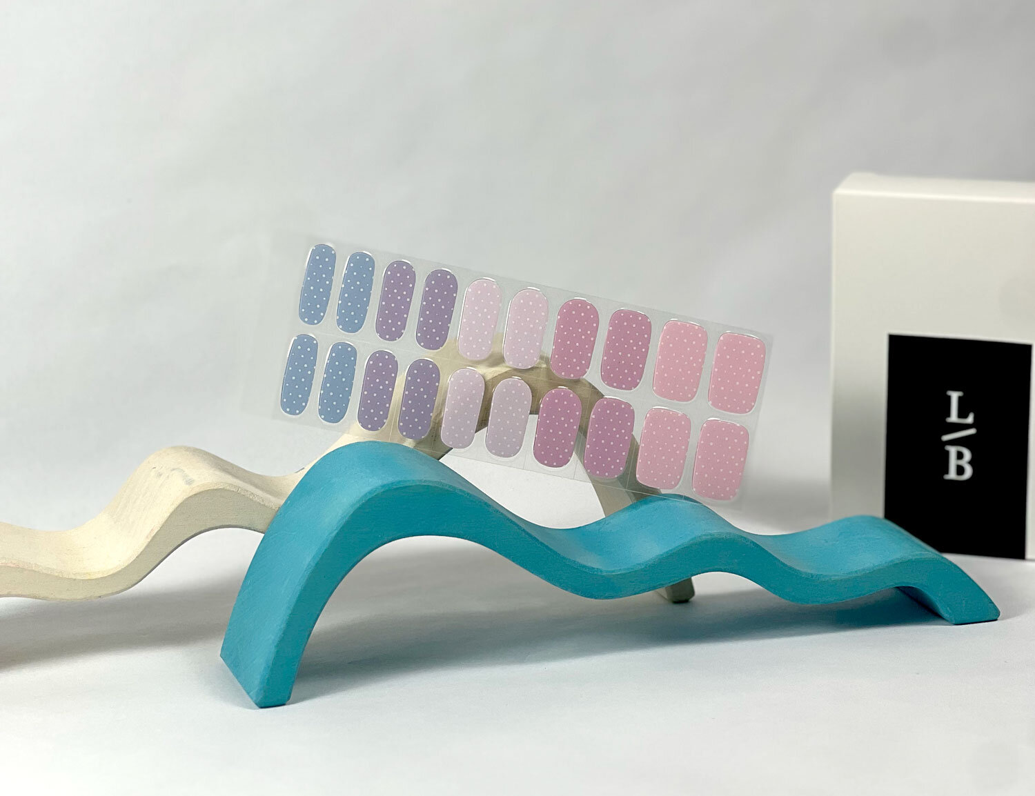 Pastel Polka Dots semi-cured gel nails in mockup to show product against blue and pink wave wooden blocks with la-bek uv lamp in the background