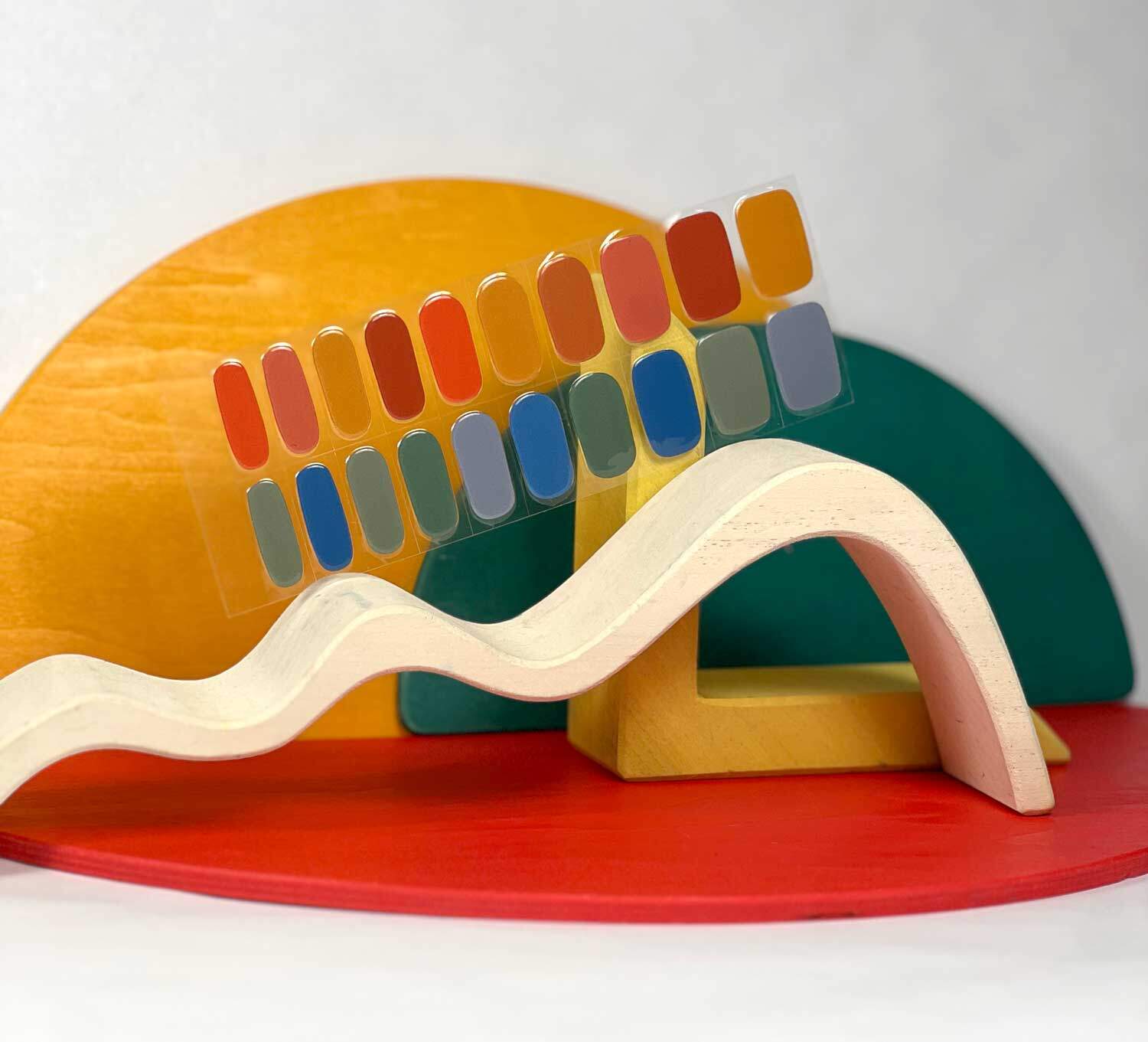 Rainbow dreams reds yellows blues semi-cured gel nails in mockup to show product against green, red and yellow wooden blocks