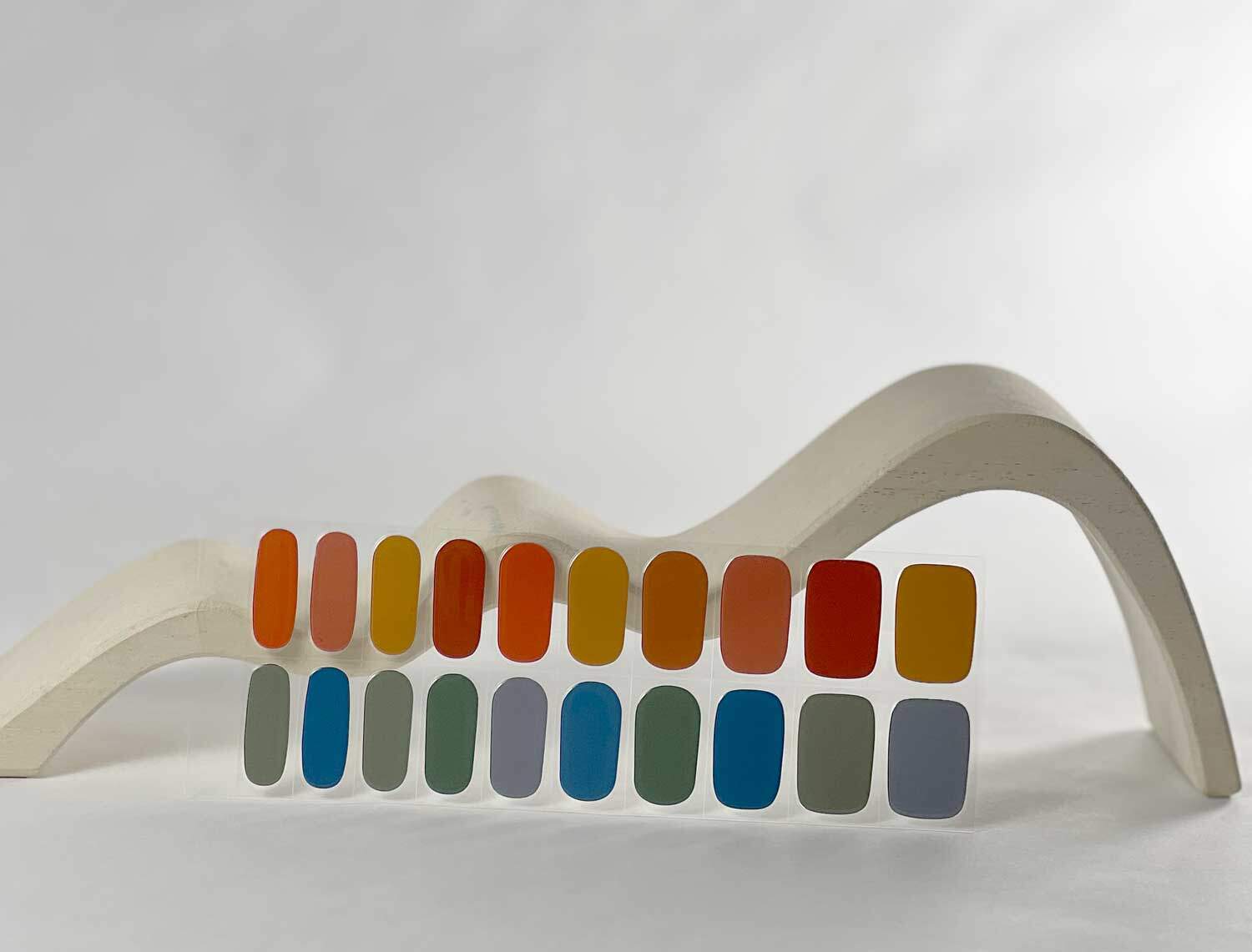 Rainbow dreams reds yellows blues semi-cured gel nails in mockup to show product against white wave wooden block