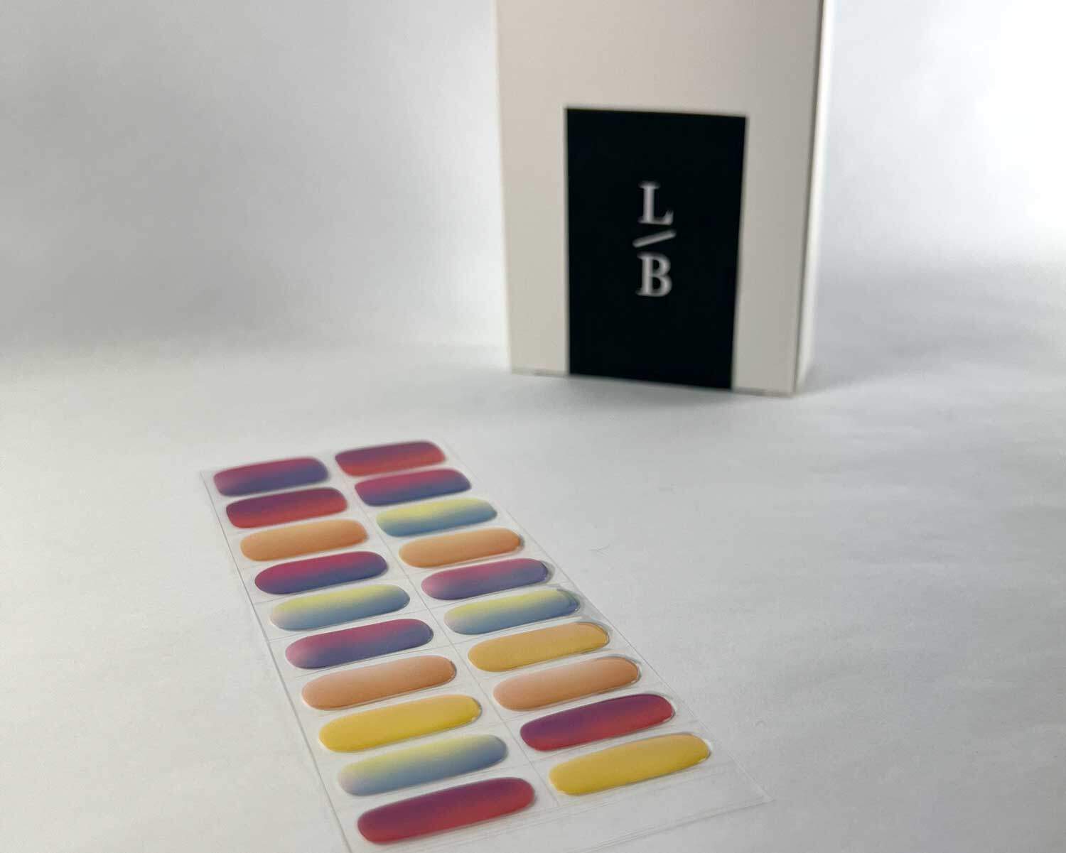 Rainbow sunset semi-cured gel nails on angle zoomed in on white background with la-bek uv lamp box in the background