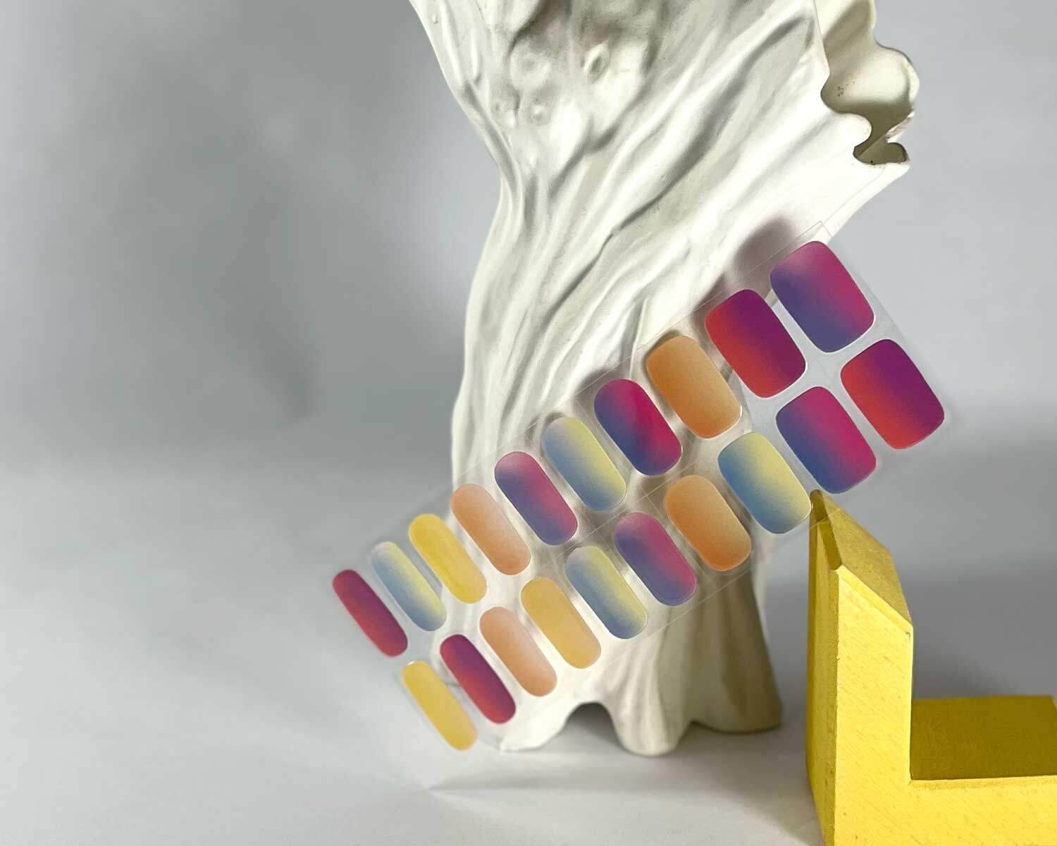 Rainbow sunset semi-cured gel nails in mockup to show product against wooden yellow block and textured white tree