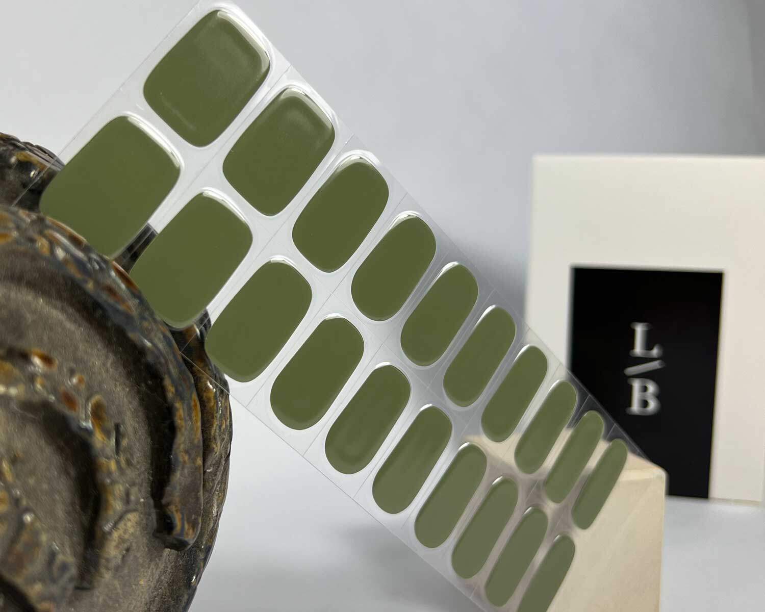 Olive green semi-cured gel nails in mockup to show product against wooden block and ceramic head with la-bek uv lamp in the background