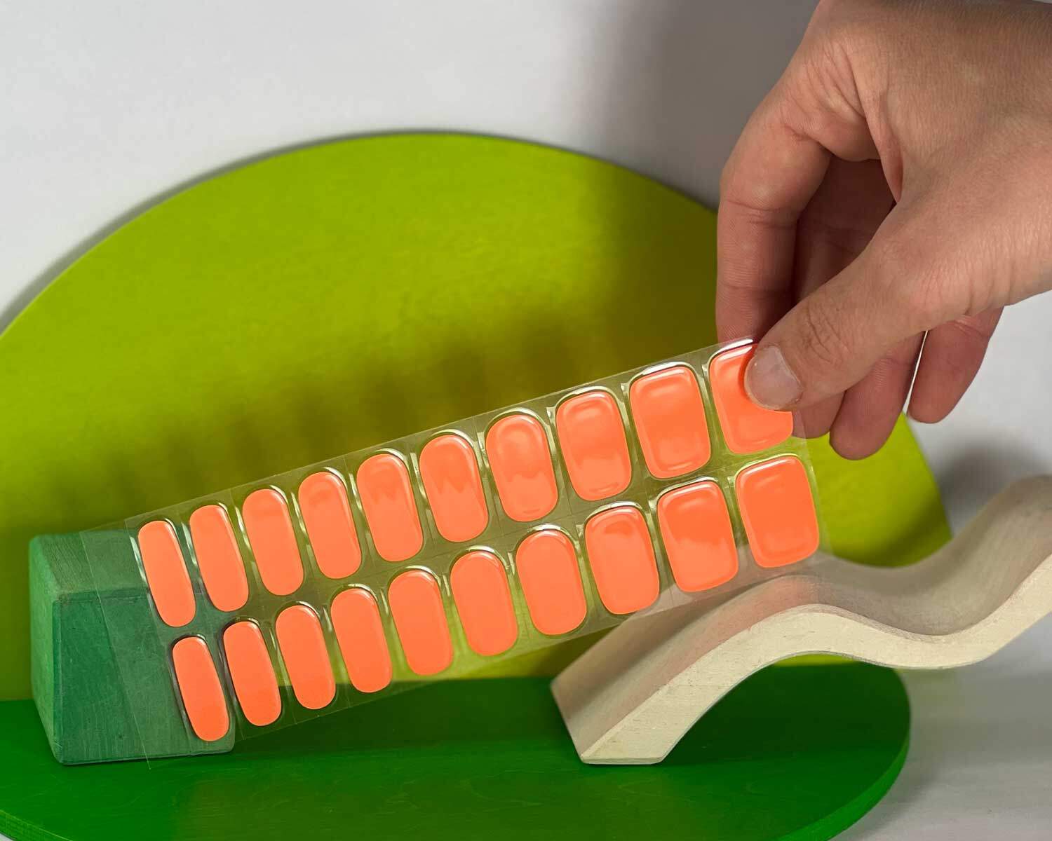 Neon Orange Glow in the dark semi-cured gel nails in mockup to show product against green and white wooden blocks