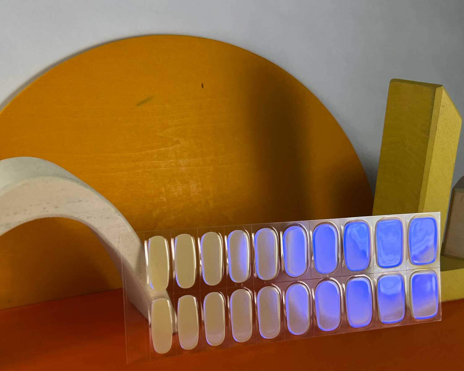 Pearlescent Lemon yellow blue semi-cured gel nails in mockup to show product against yellow, white and orange wooden blocks.