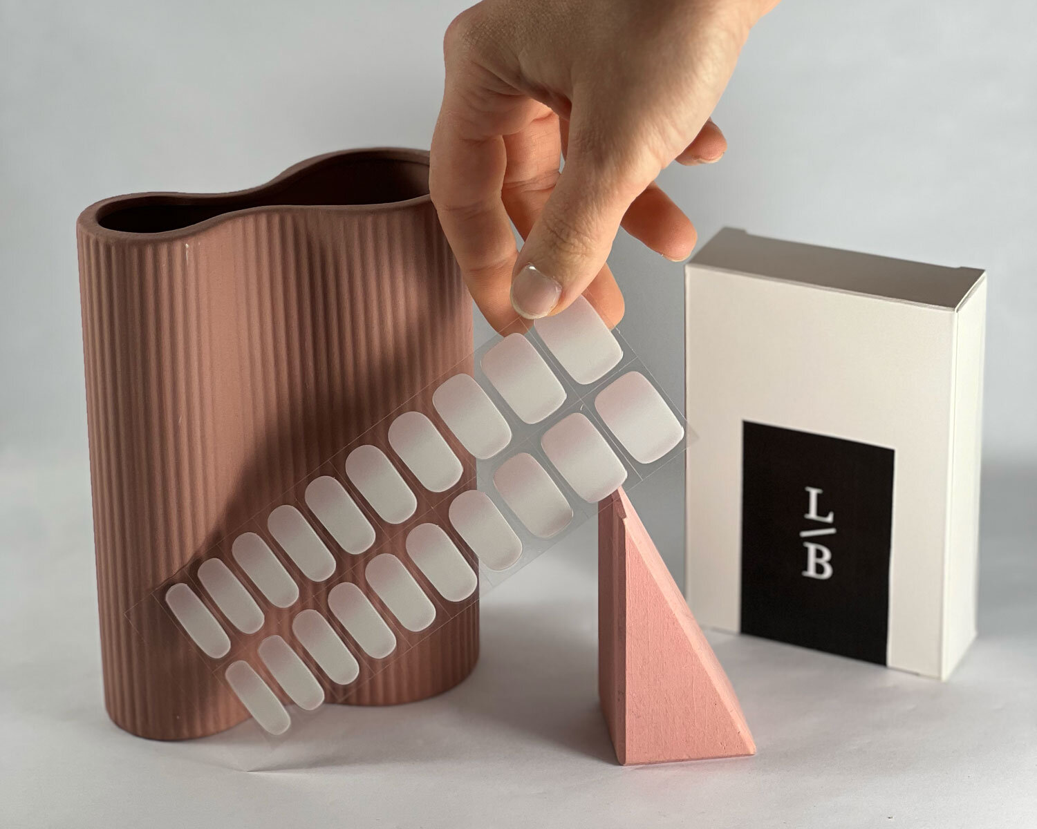 Pink Tide semi-cured gel nails in mockup to show product against pink wooden block and ceramic vase with la-bek uv lamp in the background