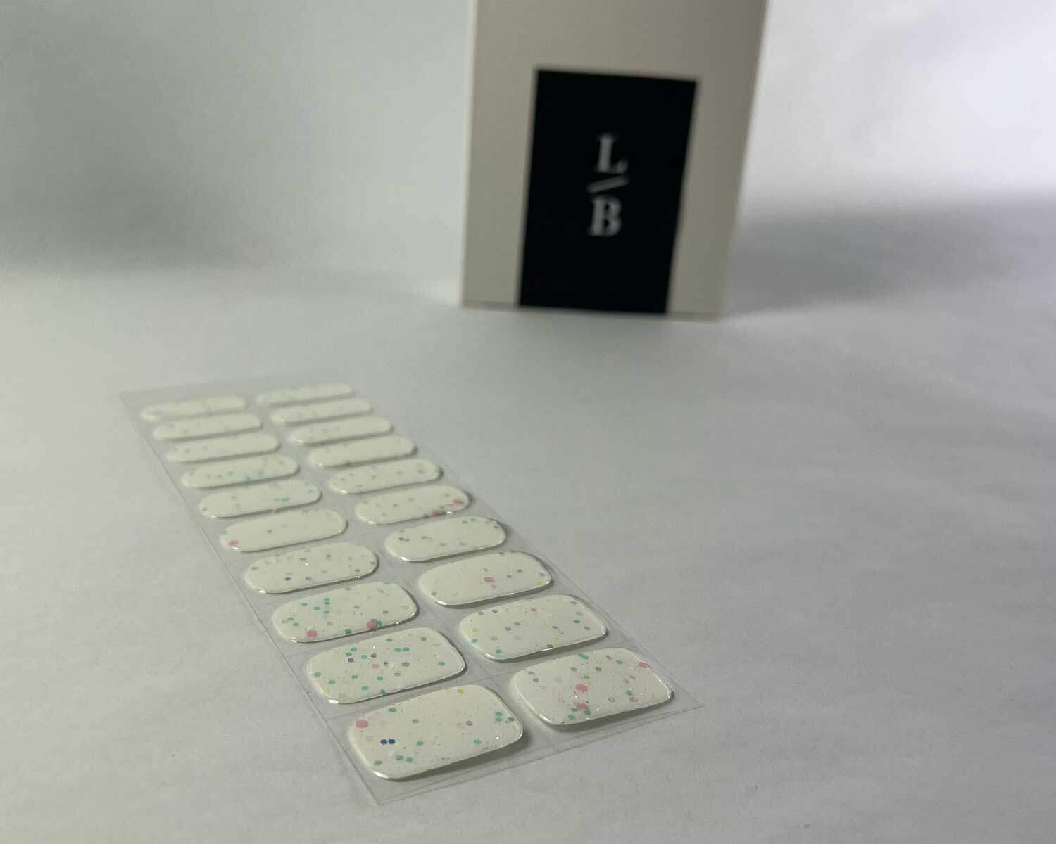 Sprinkle snow Glow in the dark white semi-cured gel nails on angle zoomed in on white background with la-bek uv lamp box in the background