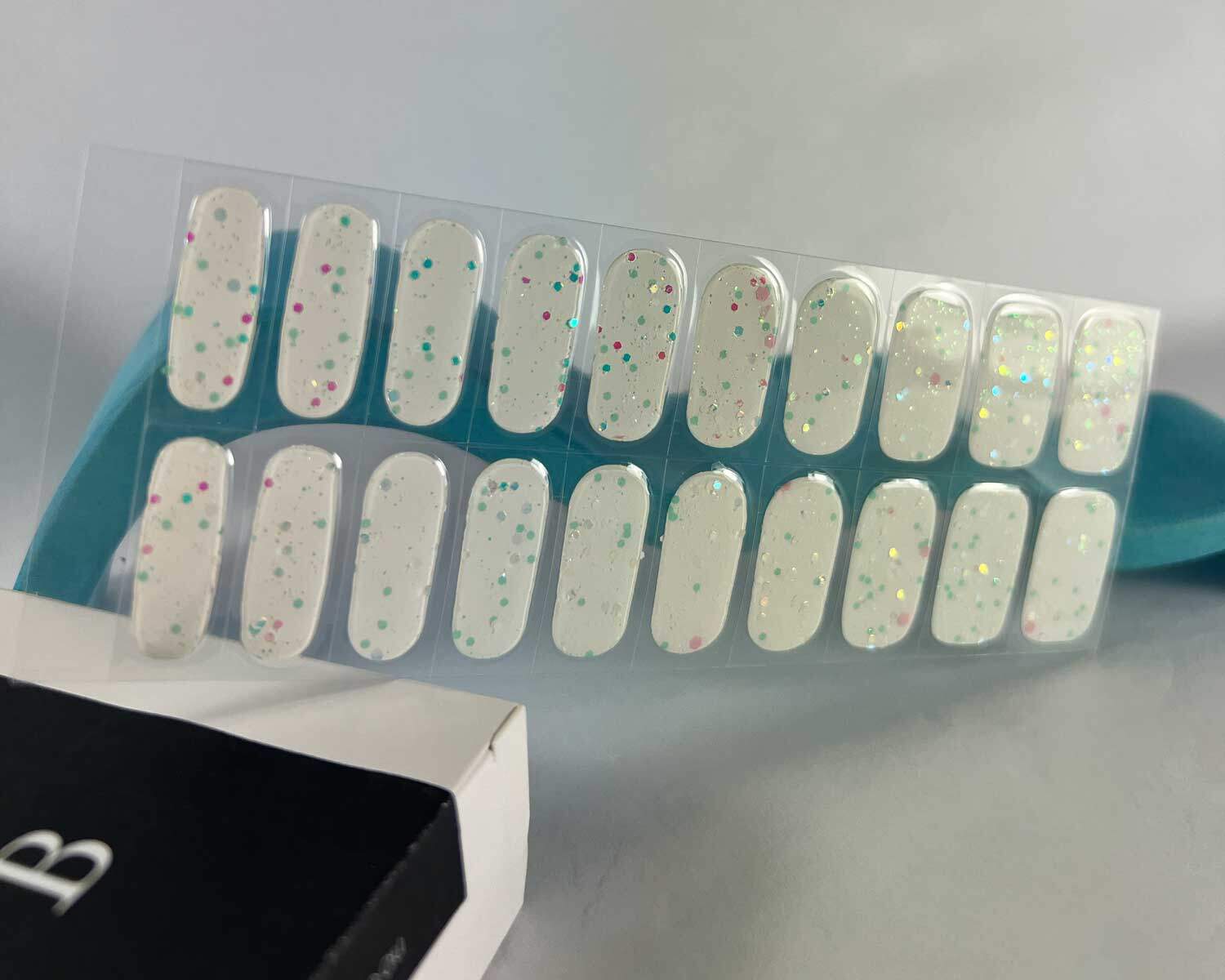 Sprinkle snow Glow in the dark white semi-cured gel nails in mockup to show product against blue wave wooden block with la-bek uv lamp in the background