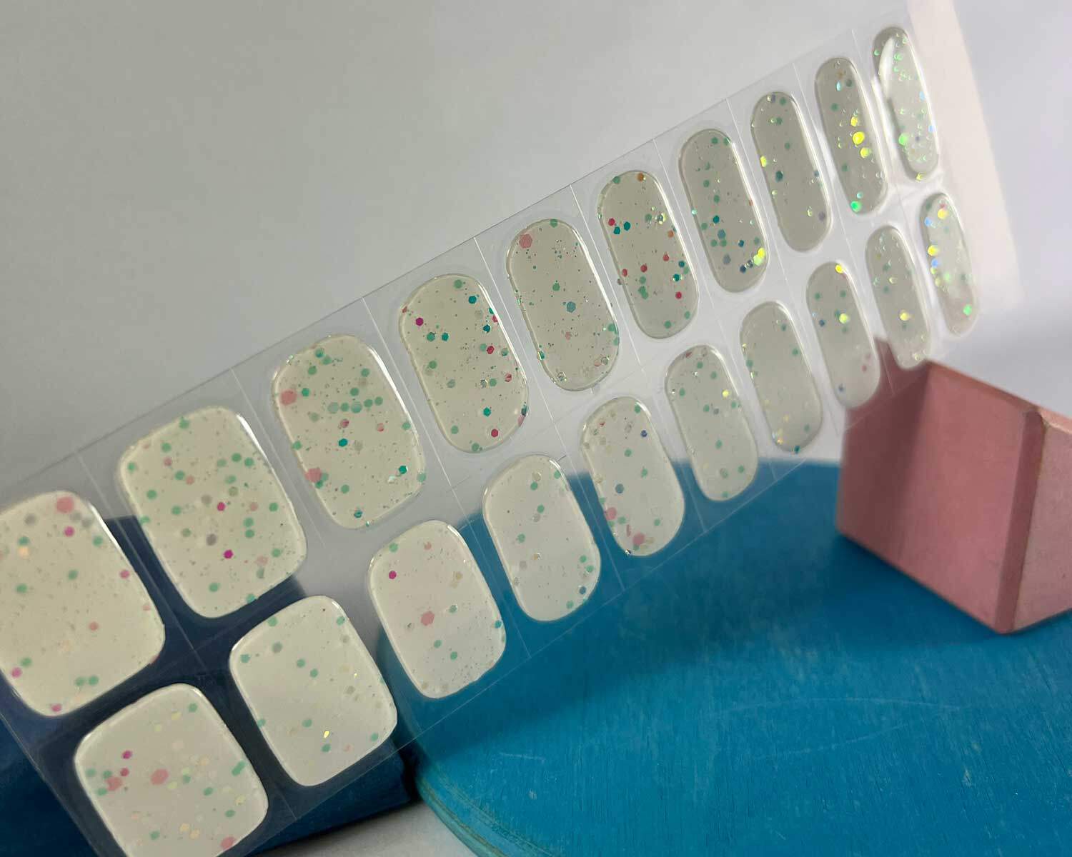 Sprinkle snow Glow in the dark white semi-cured gel nails in mockup to show product against blue and pink wooden blocks