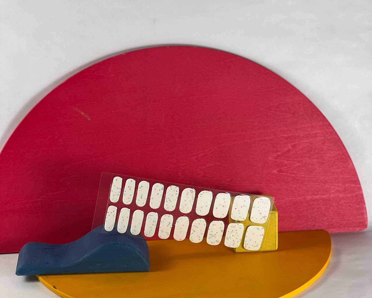 Sprinkle snow Glow in the dark white semi-cured gel nails in mockup to show product against blue, red and yellow wooden blocks