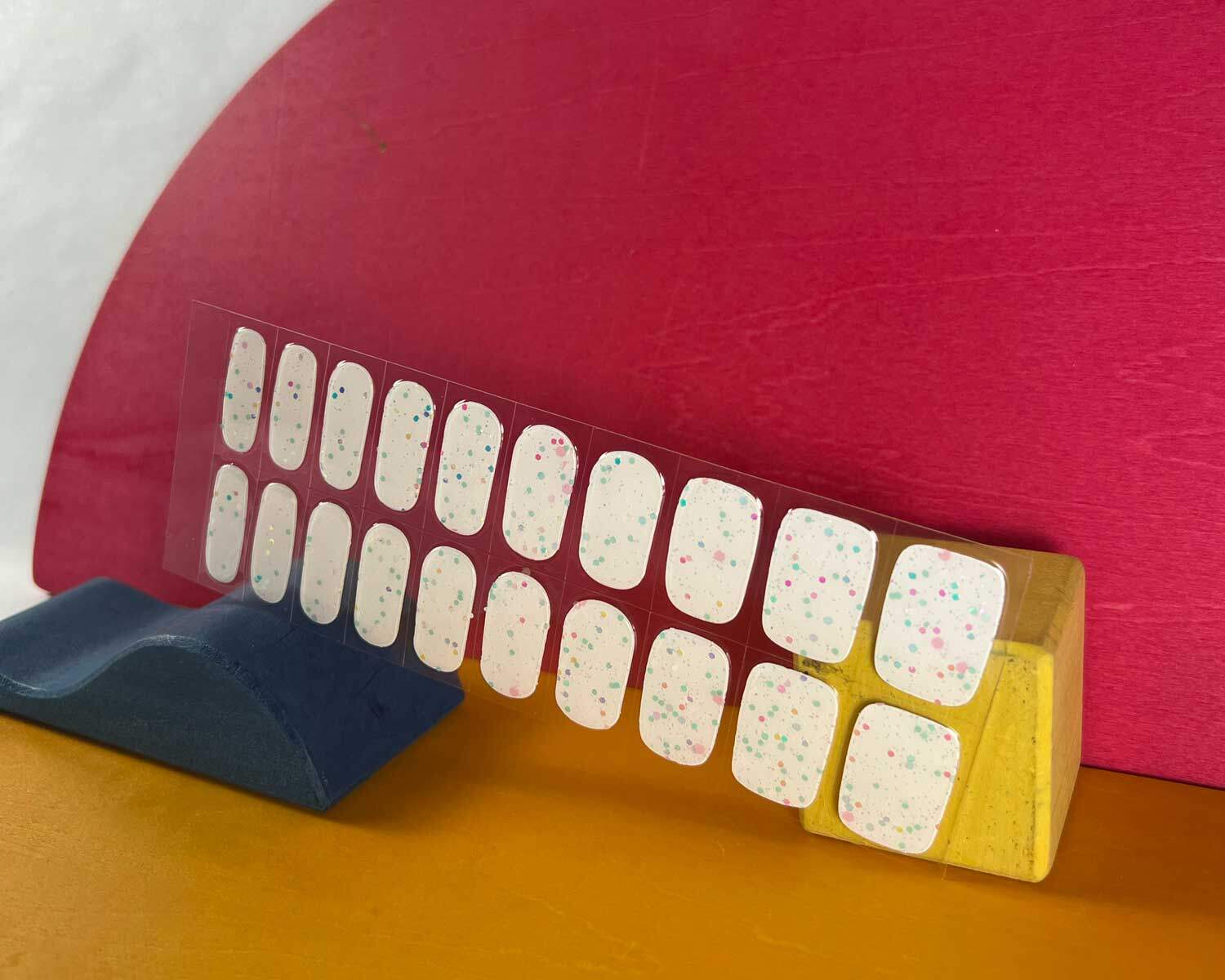 Sprinkle snow Glow in the dark white semi-cured gel nails in mockup to show product against red, yellow and blue wooden blocks