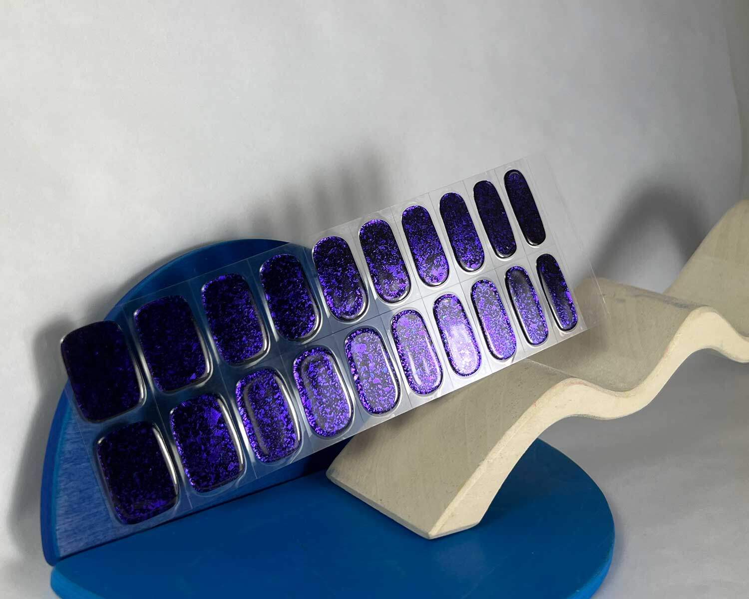 Violet Luster black and purple semi-cured gel nails in mockup to show product against white curved wooden block and blue